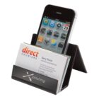 A business card holder displaying business cards in front and an iPhone behind them. The holder is a sleek, black plastic design with a logo at the bottom. The phone screen shows several app icons.