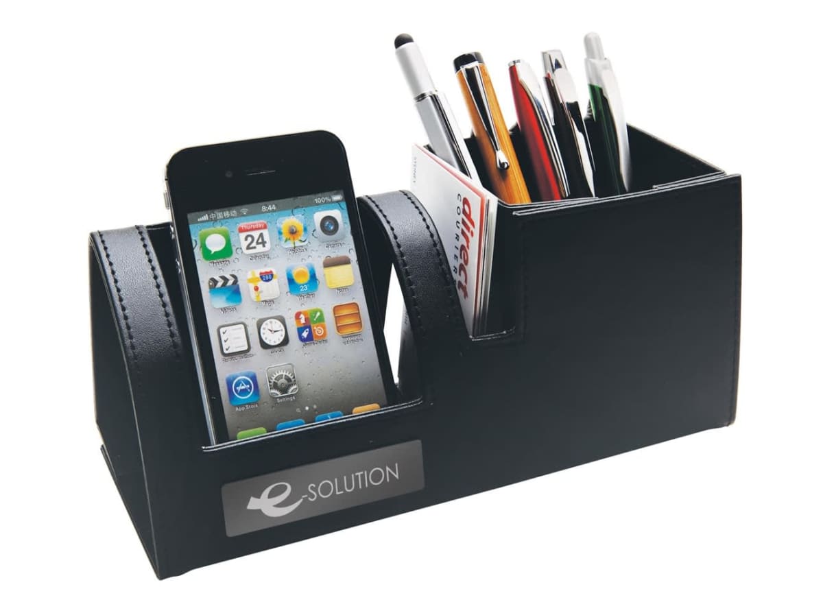 A black desk organizer holds a smartphone with its screen facing forward, and multiple pens and cards in a separate compartment. The organizer has e-Solution printed on the front.