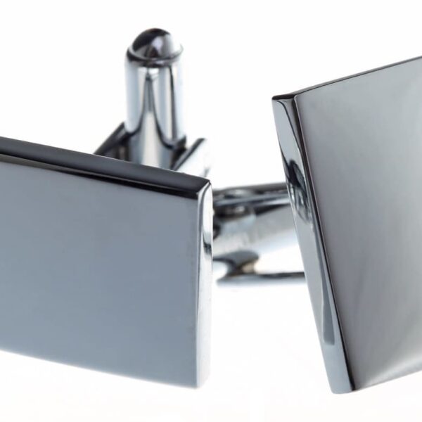 A pair of sleek, rectangular silver cufflinks with a reflective surface, positioned against a plain white background. The cufflinks are slightly tilted, highlighting their shiny finish and minimalist design.