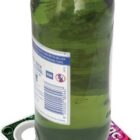 A green glass bottle with a blue cap sits on a square, colorful coaster. The coaster has a water droplet design in shades of blue, pink, and green. The bottle has a label with text and barcodes visible on one side.