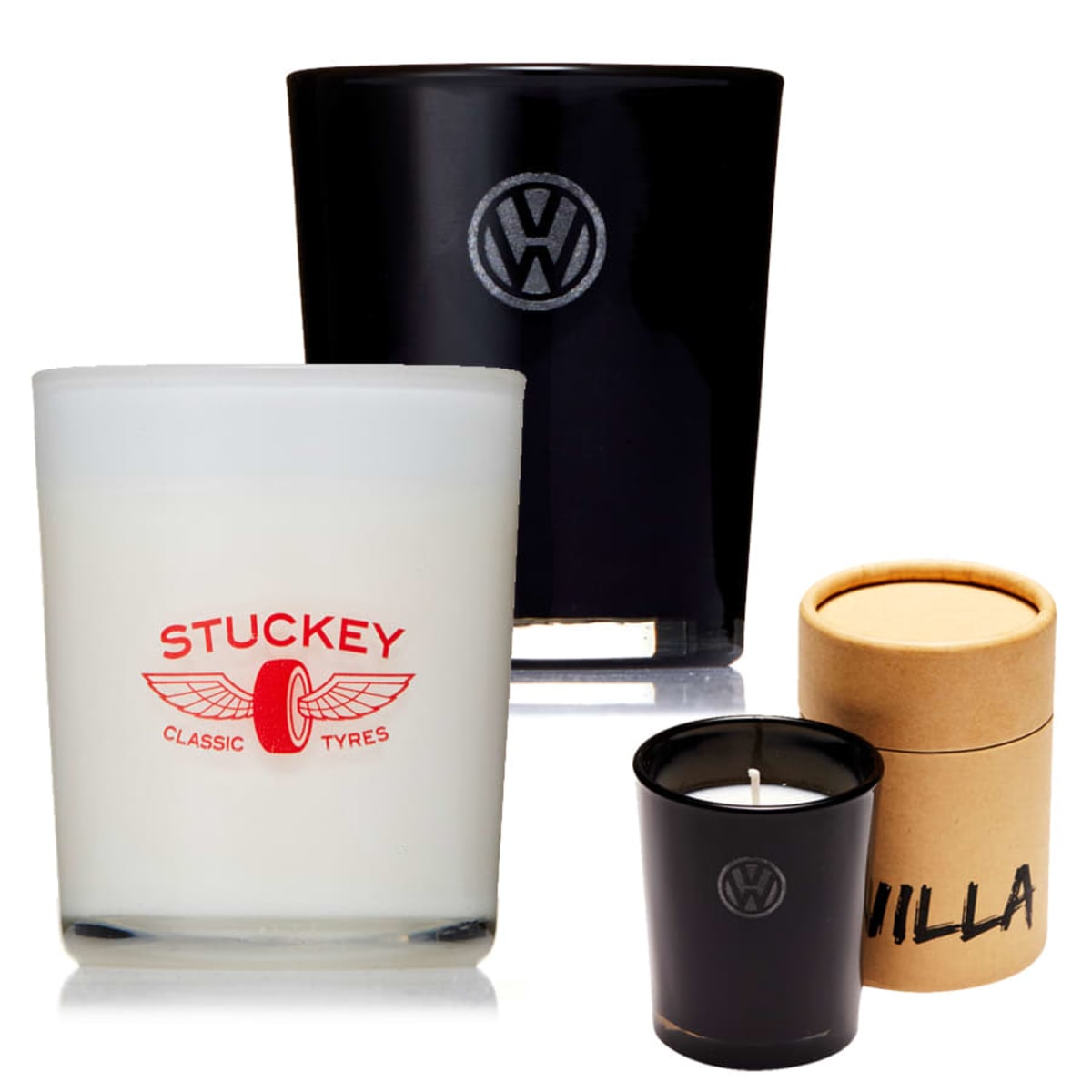 Two branded candles: one white in a clear glass with Stuckey Classic Tyres logo, and one black with a VW logo. A small black candle in front has the same VW logo. A brown cylindrical packaging labeled Vanilla is also shown.