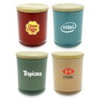 Four jars with wooden lids, each labeled with a different brand: a red jar with a yellow and red logo, a blue jar with a white logo, a green jar with a white logo, and a beige jar with a red and white logo.