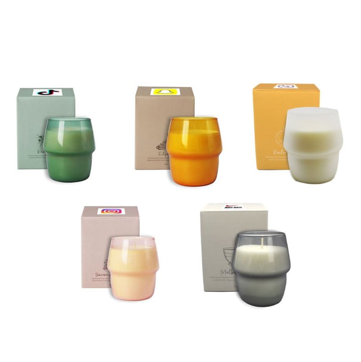 Five scented candles in different colored glass containers are placed in front of their matching boxes. The candles are green, orange, cream, pink, and gray, each with branding and labeling on the boxes.