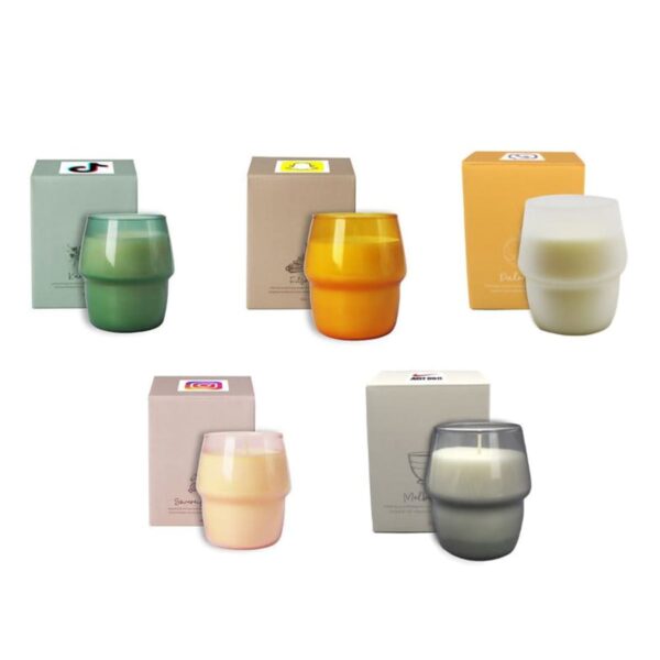 A collection of five candles in colored glass holders, each placed next to a box. The candles are green, orange, cream, peach, and gray, each with a corresponding box of similar design and color theme.