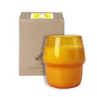 A vibrant orange candle in a curved glass holder is placed in front of a beige box. The box has a minimalist design with a Snapchat logo on top. The candle and box create a warm, inviting aesthetic.
