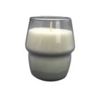 A cylindrical white candle in a clear, slightly tapered glass holder with a rounded midsection. The wick is centered at the top of the candle. The background is white.
