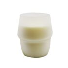 A white, cylindrical candle in a simple, modern container with smooth contours, set against a plain white background.