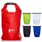 A collection of waterproof dry bags in various colors: a large red bag with GDX Creatives logo in front, and smaller green, white, black, and blue bags with different logos. Each has a roll-top closure and buckle.