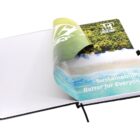 An open notebook with a page partially flipped, revealing an image of a beach with blue water and green forest. The page has the text Sustainability Better for Everyone and a logo at the top.
