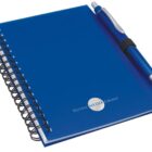A blue spiral notebook with a silver logo reading Global Media Group on the cover. A blue and silver pen is attached to the notebook with an elastic band.