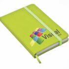 A lime green notebook with rounded corners and a matching elastic band. The cover has colorful square graphics and partially visible text starting with Visual. A ribbon bookmark is tucked inside.