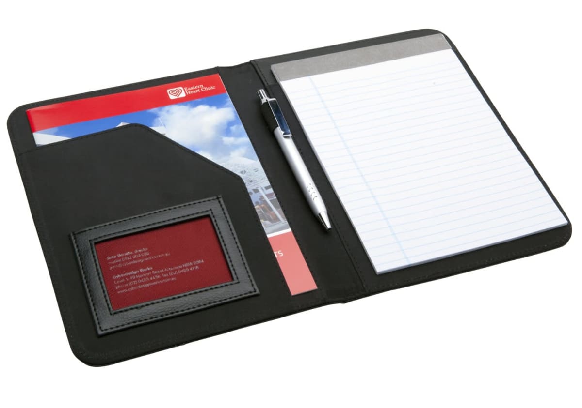 An open black portfolio with a notepad on the right, a silver pen in a holder, and pocket on the left holding a red brochure and a badge.