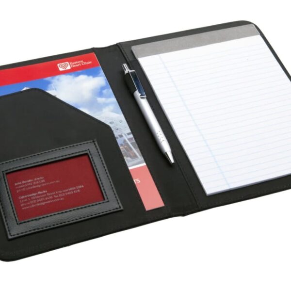 Open leather folio with a lined notepad, silver pen, business card holder, and a red pamphlet. The folio is black and neatly organized, suitable for professional use.