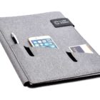 A grey portfolio organizer with three pockets on the front, holding a pen, a smartphone, and a business card. The organizer has a small black tab with white text on the upper right corner.
