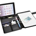 An open organizer features a tablet on the left side, several cards, a pen, and a phone in a pocket. On the right is a lined notebook page with a smartphone resting on it.