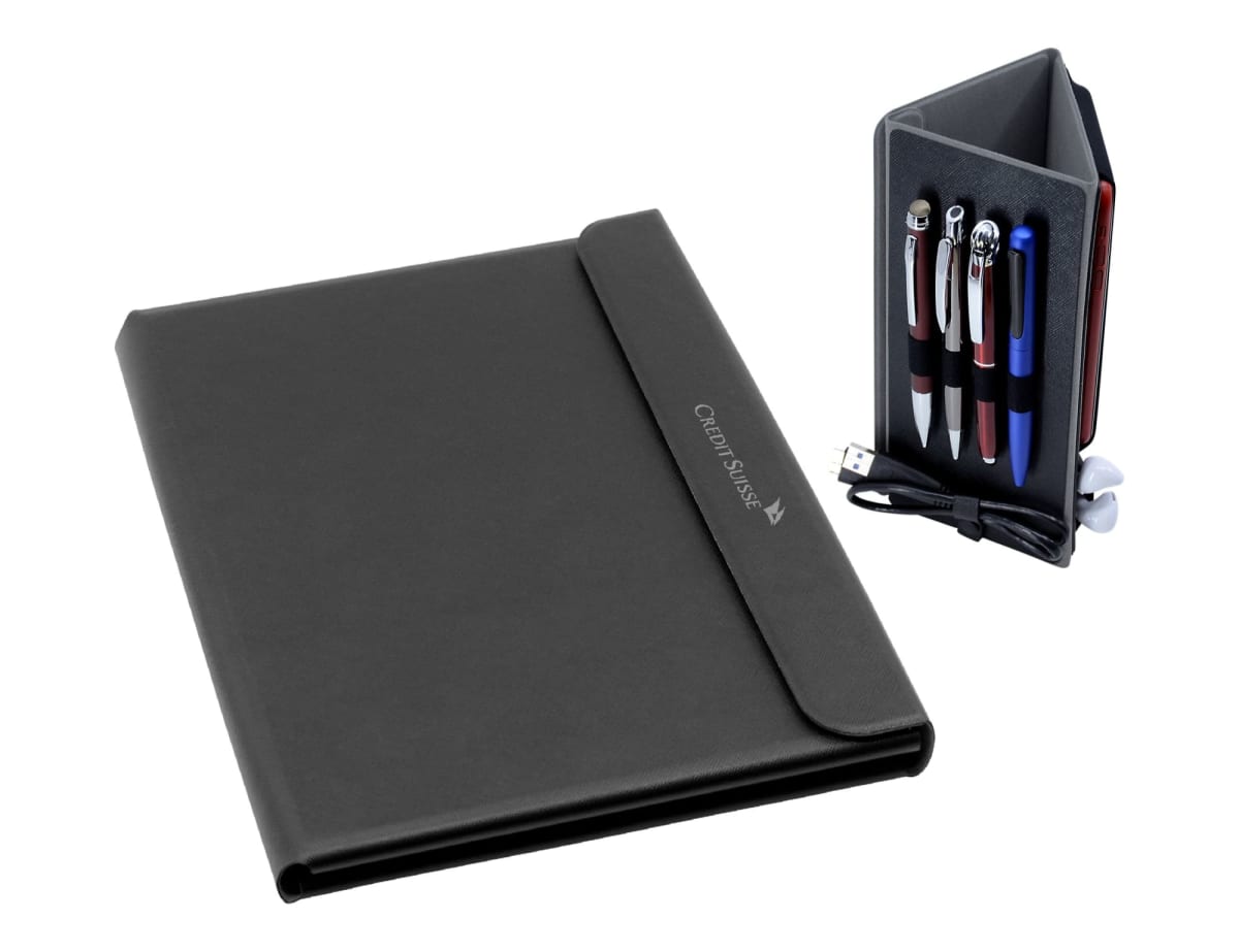 A black leather portfolio cover is on the left, displaying the engraved text CREDIT SUISSE. To the right, a small black organizer holds four pens, a USB cable, and a pair of white earbuds.