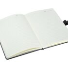 An open lined notebook with a black cover and a ribbon bookmark lies on a white surface. The pages have space for the date at the top, and the notebook is slightly angled to the left.