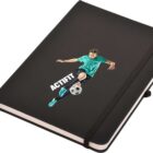 A black notebook with an elastic band and a ribbon bookmark. The cover features an illustration of a soccer player in turquoise gear kicking a soccer ball, with the text ACTIFIT beside the player.