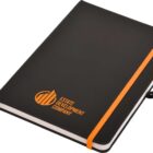 A black notebook with an orange elastic band and a logo reading Estate Development Company in orange on the cover. The notebook includes a pen holder and a ribbon bookmark.