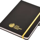A black notebook with a gold elastic band and a logo featuring the text Estate Development Company in gold. The notebook is closed and has a ribbon bookmark.