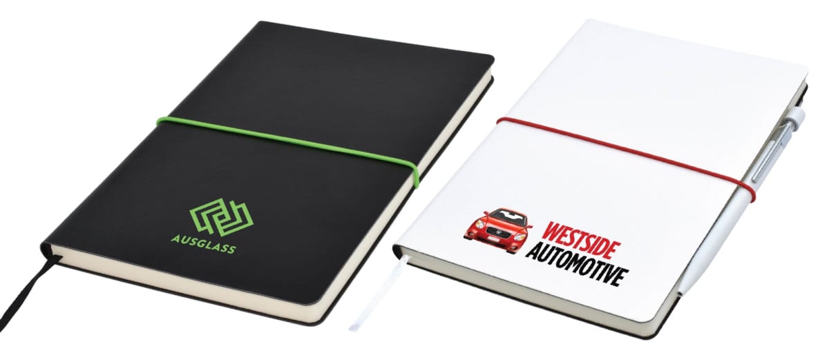 Two notebooks with elastic bands. The black notebook has a green band and the AUSGLASS logo. The white notebook has a red band, a car graphic, and the WESTSIDE AUTOMOTIVE logo. A pen is attached to the white notebook.