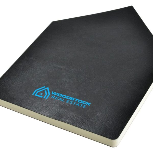 A black notebook with Woodstock Real Estate and a blue logo on the cover, featuring a minimal design. The notebook is angled slightly, showing its white pages.