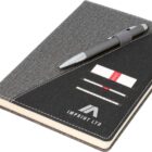 A gray notebook with a cloth cover, featuring a black diagonal section with three card slots, a pen holder, and a pen. The logo IMPRINT LTD is printed on the black section, and a gray ribbon bookmark is visible.
