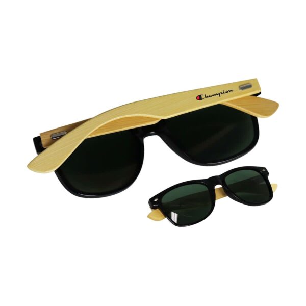 A pair of sunglasses with black lenses and bamboo-style yellow arms, featuring the Champion logo in black and red on the arms. The glasses are folded, showcasing both the front and top view.