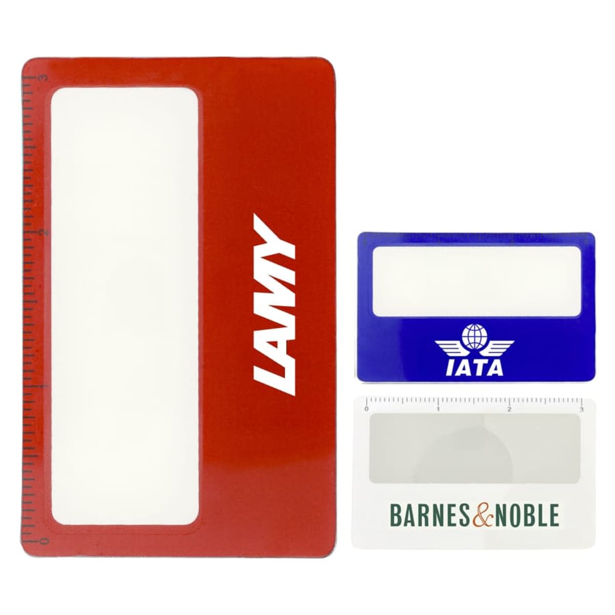 A large red rectangular magnifying card with LAMY written in white, alongside smaller blue and white magnifying cards with IATA and BARNES & NOBLE logos. The red card has a ruler on the left edge.