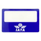 Blue magnifying card with a clear lens in the center. The bottom features the IATA logo with wings and a globe, and the word IATA below. A measuring scale runs along the top edge.