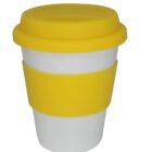 A white reusable cup with a yellow silicone band and lid. The lid has a smooth texture and fits securely on the top. The band wraps around the cup, providing grip. The cup has a minimalist design and smooth finish.
