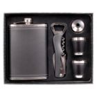 A gift set featuring a flask with a screw cap, a multifunctional bottle opener with a corkscrew, two metal shot glasses, and a funnel, all arranged neatly in a black box.