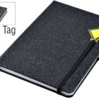 A black sparkly notebook with a black elastic band and a yellow diamond-shaped logo tag on the cover. The notebook is closed, and theres a ribbon marker. An inset shows a close-up of the logo tag.