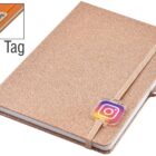 A glittery gold notebook with a beige elastic band featuring the Instagram logo. A small tagged logo is attached to the band. The notebook includes a matching ribbon bookmark.