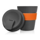 A charcoal gray reusable coffee cup with a closed lid is next to another cup showing the open mouth for drinking. Both cups have an orange grip band around the middle.