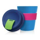 A blue reusable coffee cup with a dark blue lid and a green flip-up tab. The cup has a pink silicone band around its middle. The lid is placed slightly leaning against the cup.
