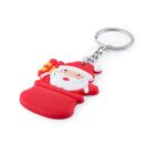 A keychain featuring a smiling Santa Claus figure, holding a yellow gift. Santa is wearing his traditional red outfit and hat. The keychain has a metal ring attached. The background is plain white.
