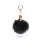 A black fluffy pom-pom keychain with a gold clasp and a small gold tag attached. The pom-pom appears soft with a dense texture, hanging freely against a plain white background.