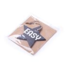 A wooden star-shaped ornament with the word EASY is enclosed in a clear plastic wrapper. It is attached to a piece of brown cardboard and has a jute string loop at the top for hanging.