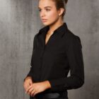 A person with brown hair is standing against a gray textured background. They are wearing a black button-up shirt and dark pants, looking to the side with a neutral expression.