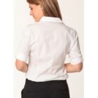 A woman with long hair is seen from the back, wearing a white dress shirt and black pants. The shirt sleeves are rolled up, and she stands against a plain background.