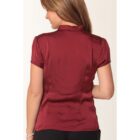 A woman with brown hair is facing away, wearing a short-sleeved, maroon satin blouse and black pants against a plain background.