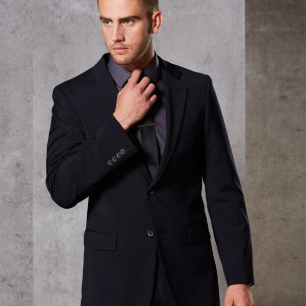 A man in a dark suit and tie stands against a gray textured wall. He is adjusting his tie with one hand and looking off to the side with a thoughtful expression.