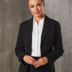 A person wearing a black blazer and white shirt, standing with their hands clasped in front. The background is a textured gray surface. The person has a neutral expression and neatly styled hair.