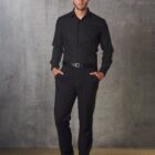 Man in black shirt and pants stands against a textured gray wall.