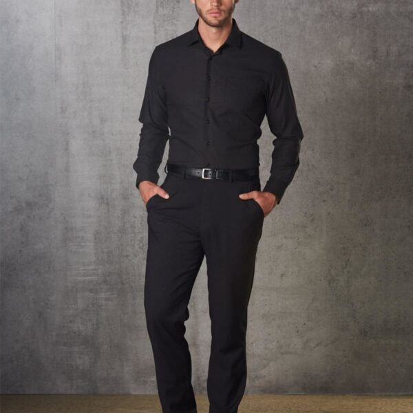 Man in black shirt and pants stands against a textured gray wall.