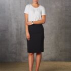 A woman stands against a gray textured wall. She wears a white shirt, black skirt, black high heels, and a watch on her left wrist. Her hair is neatly tied back, and she stands with her arms gently crossed.