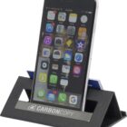 A smartphone displaying various app icons is propped up on a black triangular phone stand. The stand has a silver plate with the logo and text CARBON COPY.