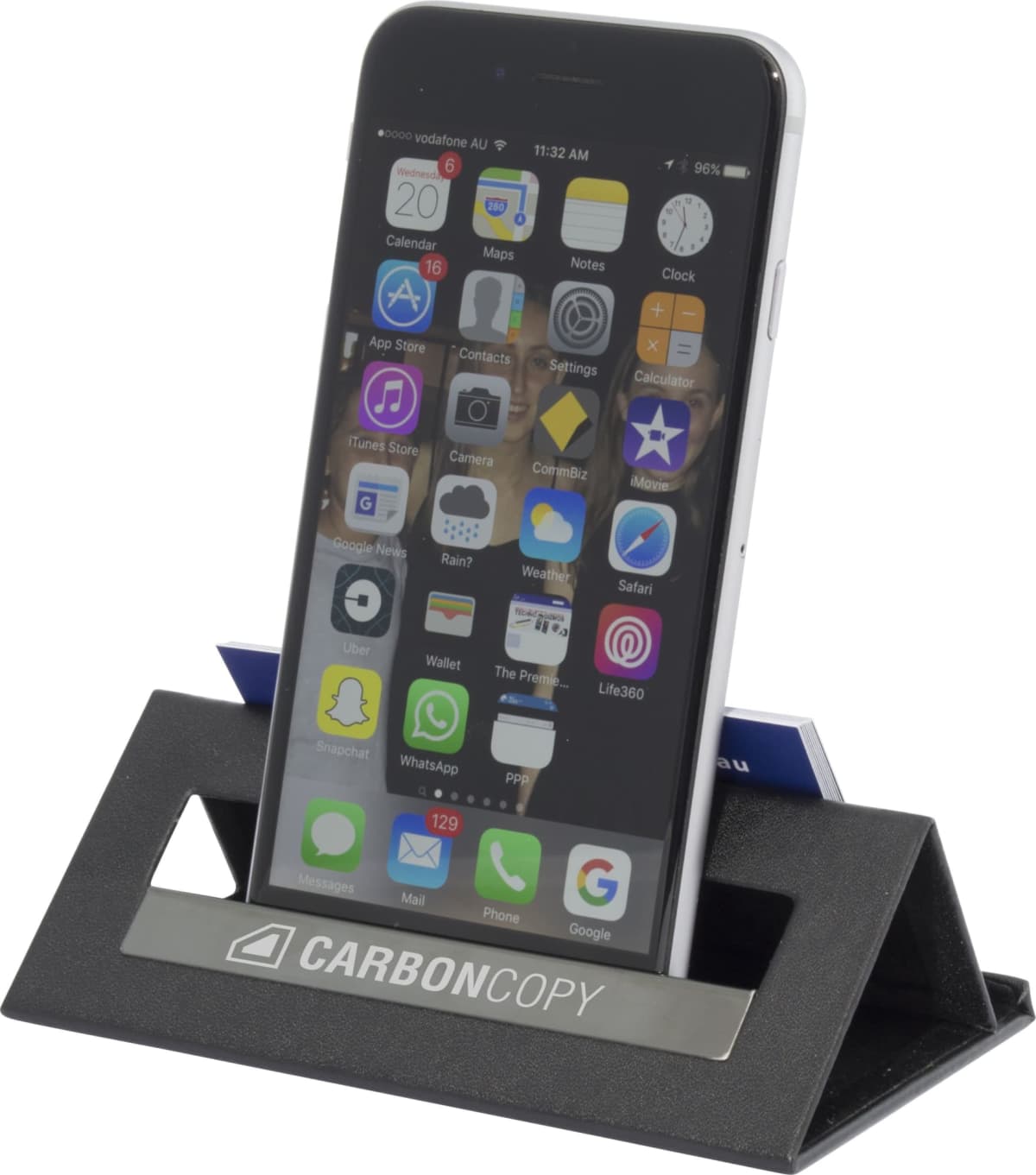 A smartphone displaying various app icons is propped up on a black triangular phone stand. The stand has a silver plate with the logo and text CARBON COPY.