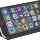 A smartphone with a case is propped on a stand. Its screen displays various app icons including mail, music, and social media on a floral wallpaper background.